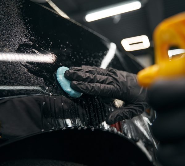 Cropped photo of skilled worker in nitrile gloves pressing lump of clay to car surface