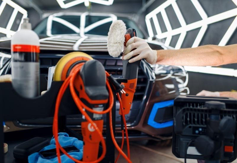 Worker, polishing machine and tools, car detailing Male worker near toolbox with polishing machine and polish tools, car detailing. Preparationa before installation of coating that protects the paint of automobile from scratches, auto tuning